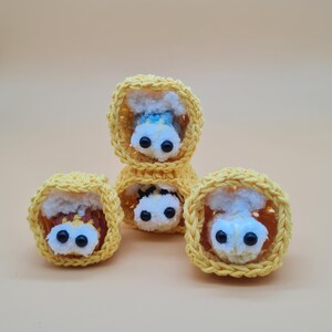 May include: A collection of handmade crochet sushi pieces. Each piece features a yellow crocheted exterior, with a white and brown interior, and black bead eyes. The sushi pieces are arranged on a light orange background.