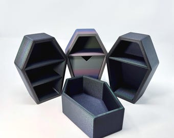 May include: Four coffin-shaped storage containers in various sizes and designs. The containers are dark with a subtle iridescent sheen. One has shelves, another a drawer, and the last is open. The containers are on a white background.