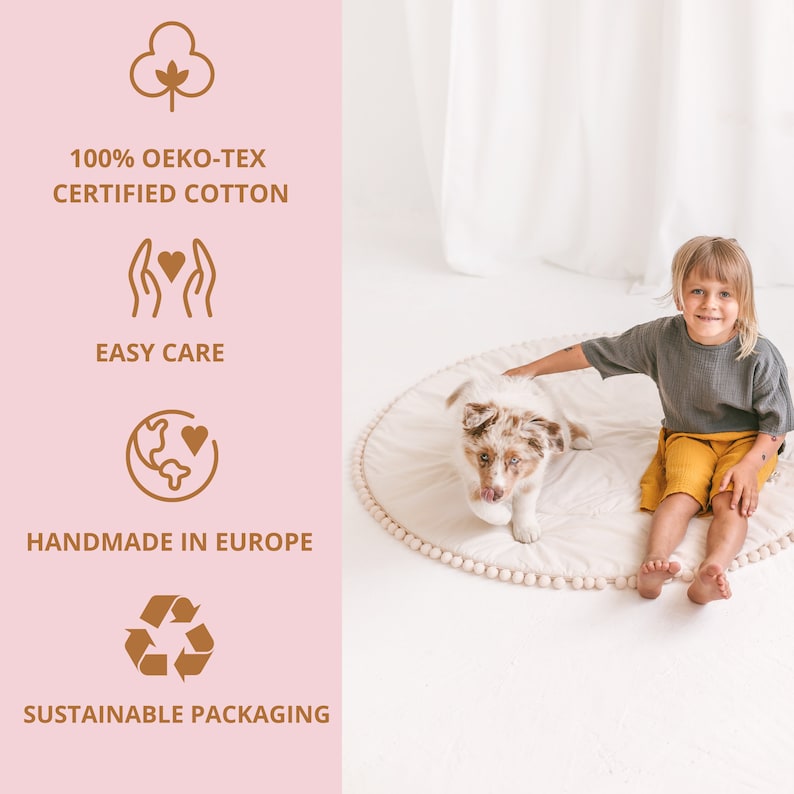 May include: A white play mat with a brown pom-pom border. A child is sitting on the mat with a puppy. The mat is made of 100% Oeko-Tex certified cotton, is easy care, handmade in Europe, and comes in sustainable packaging.