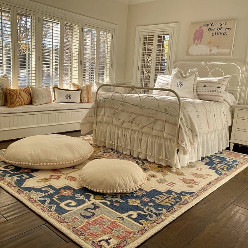 May include: A white metal bed frame with a white and pink striped comforter and a white ruffled bed skirt. The bed is in a bedroom with a white wainscoting and a rug with a blue and cream pattern. There is a sign above the bed that says "Hey You, Get Off Of My Cloud."