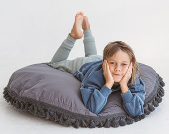Peut inclure: Un coussin de sol rond gris avec une frange décorative à pompons sur le bord. Le coussin est fait d'un tissu doux et est conçu pour le confort. Un ajout élégant à tout espace de vie, environ 100 cm de diamètre.