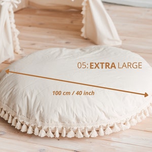 May include: A large, round, cream-colored cushion with a white fringe border. The cushion measures 40 inches in diameter. The text "05: EXTRA LARGE" and "100 cm / 40 inch" is printed on the cushion.