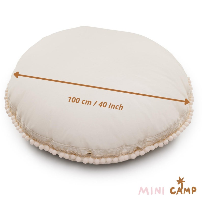 May include: A large, round, cream-colored floor cushion with a white pom-pom trim. The cushion measures 40 inches in diameter.