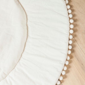 May include: A white round play mat with a white pom-pom trim around the edge.