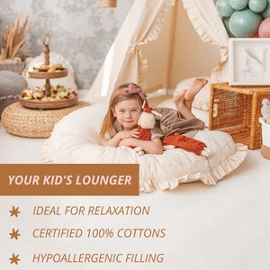May include: A white and beige children's lounger with a ruffled edge. A young girl is sitting on the lounger with a stuffed animal. The lounger is ideal for relaxation and features a removable cover and hypoallergenic filling.