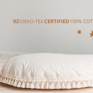 May include: A large, round, white cushion with a white fringe trim and tassels. The cushion is made of 100% cotton and is OEKO-TEX certified. The text "02: OEKO-TEX CERTIFIED 100% COTTON" is visible above the cushion.