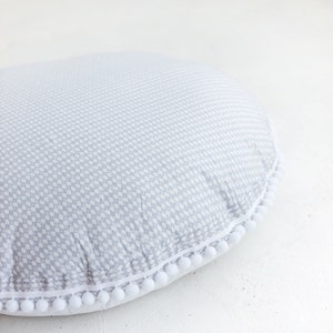 May include: A gray and white patterned floor cushion with a white pom-pom trim.