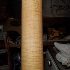 Puede incluir: Primer plano de una pieza de madera cilíndrica de color marrón claro con un patrón de veta distintivo. La madera tiene una superficie lisa y parece estar pulida.