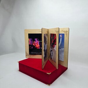 May include: A wooden photo frame with four slots for displaying pictures. The frame is decorated with a gold-coloured design and sits on a red velvet base.