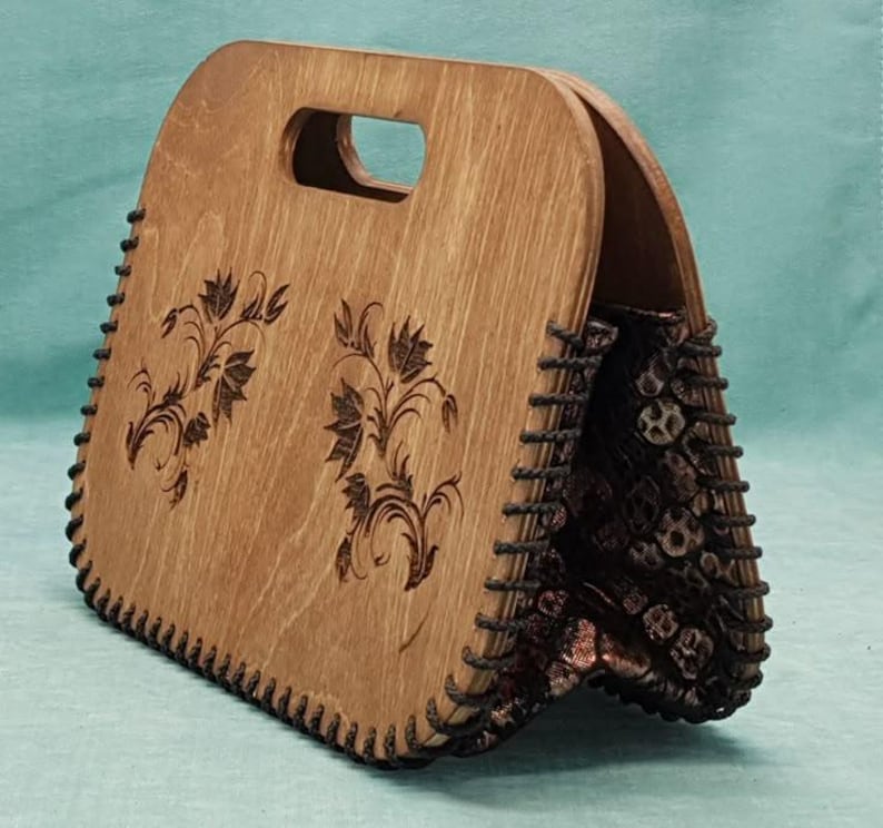Op de afbeelding: Een houten handtas met een bloemenpatroon en een zwarte stoffen voering. De tas heeft een handvat en een gestikte rand.