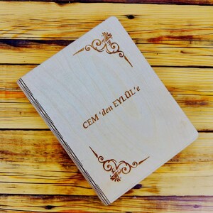 May include: A wooden box with a light brown finish and a decorative design engraved on the front. The box has the text "CEM'den EYL&Uuml;L'e" engraved on the front.