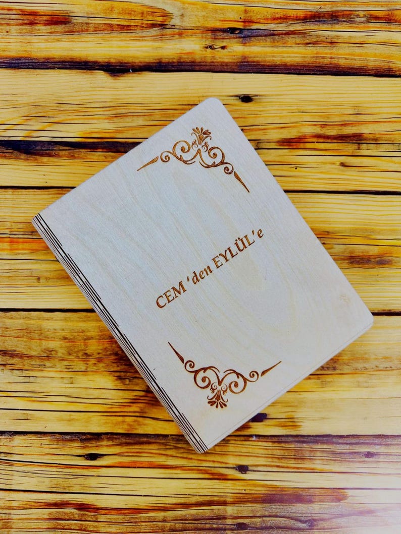 May include: A wooden box with a light brown finish and a decorative design engraved on the front. The box has the text "CEM'den EYL&Uuml;L'e" engraved on the front.