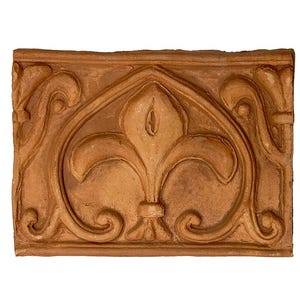 Puede incluir: Una baldosa decorativa rectangular de color terracota con un diseño de flor de lis. La baldosa tiene un patrón en relieve adornado con líneas curvas y un motivo floral central. Los bordes son ligeramente ásperos, lo que le da un aspecto rústico.