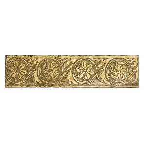 May include: A rectangular, aged-looking decorative tile with a repeating floral and scroll design. The tile features a cream-colored base with a detailed, embossed pattern in shades of gold and brown. The design includes circular floral motifs and swirling scrollwork.