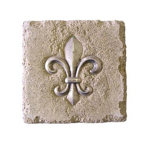 May include: A square, textured, light beige stone with a silver fleur-de-lis emblem. The emblem is centered on the stone and features a stylized design with three petals and curved accents. The stone has a rough, aged appearance.