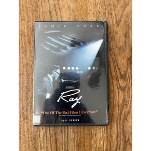 Peut inclure: Un boîtier DVD en noir et blanc pour le film Ray avec Jamie Foxx. La couverture présente la silhouette d'une personne au piano, le titre Ray en écriture blanche, ainsi que le texte One Of The Best Films I Ever Saw et FULL SCREEN.