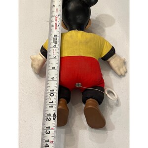 Op de afbeelding: Vintage Mickey Mouse trekspeelgoed. Het speelgoed is ongeveer 30 cm hoog. Mickey Mouse draagt een geel shirt, een rode broek, zwarte schoenen en witte handschoenen. Het speelgoed heeft een trekkoord aan de achterkant.