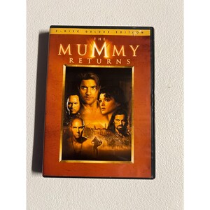 May include: A 2-disc deluxe edition DVD case for the movie The Mummy Returns. The cover features a warm orange and brown color palette with a central rectangular image displaying the film's cast members, including Brendan Fraser and Rachel Weisz.