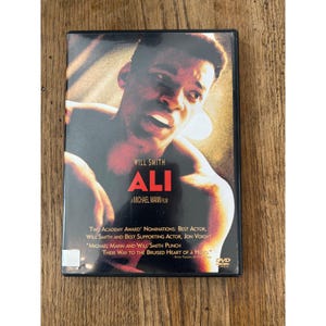 May include: DVD of the movie "Ali" starring Will Smith. The cover features a close-up of Smith's face with the title in red. The DVD case includes text about the film's Academy Award nominations and the director, Michael Mann.