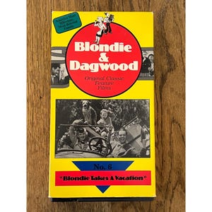 May include: A yellow VHS tape cover for Blondie & Dagwood Original Classic Feature Films No. 6, Blondie Takes A Vacation. The cover features a red circle with the title, a black and white photo of a family in a car, and a blue text box.