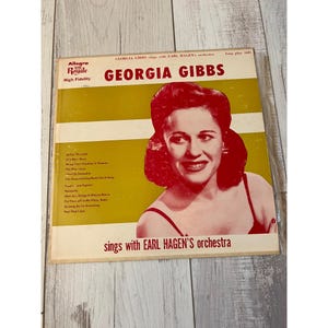 May include: Vintage vinyl record album cover featuring Georgia Gibbs, with text reading "GEORGIA GIBBS sings with EARL HAGEN'S orchestra." The album cover has a yellow and white background with a photo of Georgia Gibbs in a red dress.