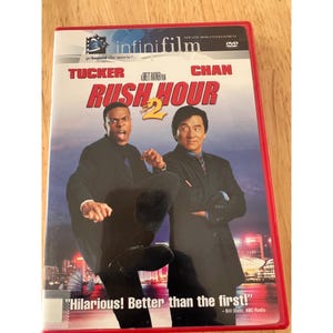 May include: A DVD case for the film Rush Hour 2, featuring actors Chris Tucker and Jackie Chan on the cover. The title is printed in red, with the text Hilarious! Better than the first! at the bottom and the infiniFilm logo at the top.