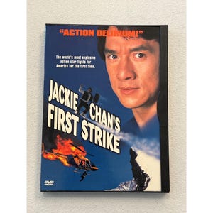 Può includere: Custodia DVD di "Jackie Chan's First Strike". La copertina presenta il volto di Jackie Chan, un elicottero e una figura che scivola giù da una montagna innevata. Il testo include "ACTION DERUM!" e "The world's most explosive action star fights for America for the first time."