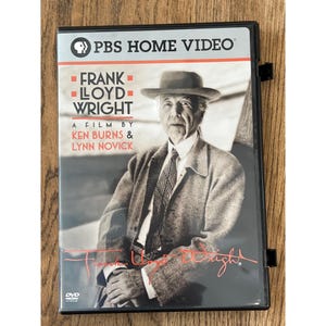 Könnte beinhalten: DVD-Hülle für "Frank Lloyd Wright: A Film by Ken Burns & Lynn Novick" von PBS Home Video. Das Cover zeigt ein Schwarz-Weiß-Porträt eines Mannes mit Hut und Mantel, mit Titel und Credits in Rot und Weiß.