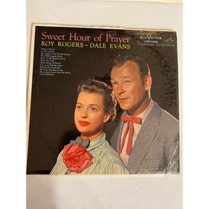 以下が含まれることがあります： ロイ・ロジャースとデール・エバンスによる「Sweet Hour of Prayer」のヴィンテージビニールレコードアルバムのカバー。カバーには、2人の歌手の肖像画が描かれています。アルバムタイトルとアーティスト名はピンク色のテキストです。RCA Victorのロゴは右上にあります。