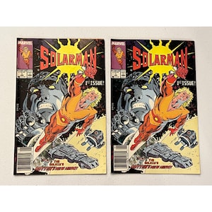 May include: Two copies of the comic book "Solarman" are displayed. The cover features a superhero in an orange and yellow suit, with a large, gray-skinned alien head in the background. The title is in large, red letters with a yellow sunburst.