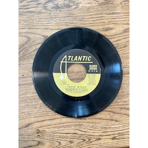 May include: A black 45 RPM vinyl record with a yellow and black Atlantic Oldies Series label. The center label features the text Trade Winds by Roberta Flack, along with production credits, the Atlantic logo, and catalog number OS-13142.