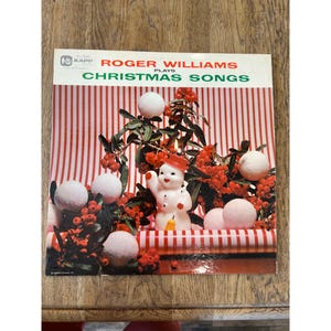 May include: A vintage vinyl record album cover featuring a snowman with a red hat and a candle, surrounded by red berries and white snowballs. The album cover is red and white striped and features the text "Roger Williams Plays Christmas Songs".
