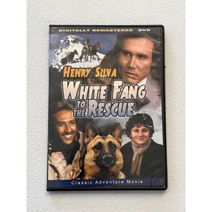 Peut inclure: DVD du film "White Fang to the Rescue" avec Henry Silva. La jaquette présente un homme, un chien et un garçon, avec une scène de montagne en arrière-plan. Le boîtier du DVD est noir.