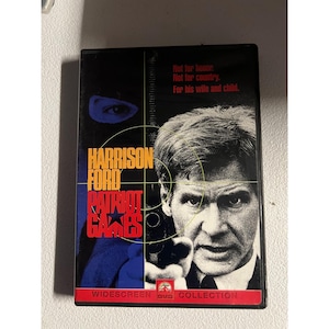 May include: DVD case for the movie "Patriot Games" starring Harrison Ford. The cover features Ford holding a gun, with text overlay including the movie title and the phrase "Not for honor. Not for country. For his wife and child."