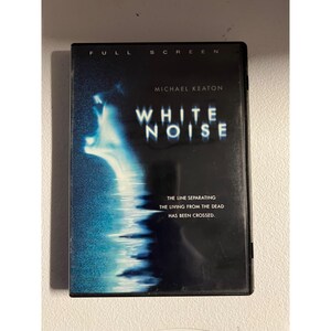 Peut inclure: Un boîtier DVD noir pour le film "White Noise" avec Michael Keaton. La couverture présente un graphisme blanc et bleu avec le titre "WHITE NOISE" en grandes lettres. Le texte "FULL SCREEN" est en haut. Le slogan est : "LA LIGNE SÉPARANT LES VIVANTS DES MORTS A ÉTÉ FRANCHIE."