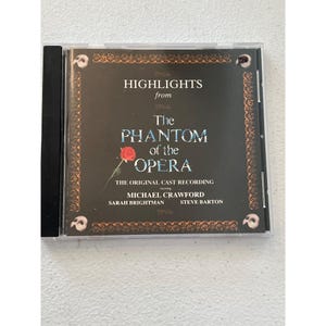 Op de afbeelding: Een cd-hoesje met "Highlights from The Phantom of the Opera". De cover is donker met de titel in een groot, gestileerd lettertype. Een rode roos is afgebeeld. De originele opname bevat Michael Crawford, Sarah Brightman en Steve Barton.