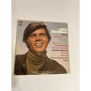 Może przedstawiać: Vintage okładka albumu winylowego z Johnem Davidsonem. Okładka albumu przedstawia portret Davidsona z tytułem albumu i tytułami piosenek, w tym "Stormy" i "Little Green Apples". Okładka jest w odcieniach brązu, beżu i niebieskiego.