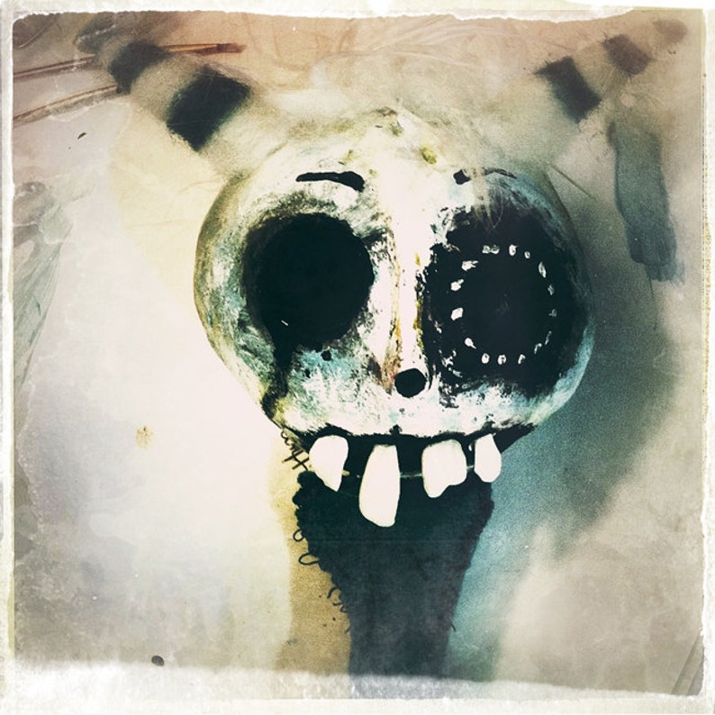 May include: A white and black painted papier-m&acirc;ch&eacute; skull with a large black eye and a toothy grin. The skull is painted with a distressed, vintage look.