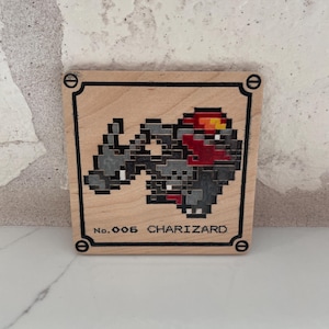May include: A square wooden plaque featuring a pixel art illustration of the character Charizard in shades of gray, red, and yellow. The text No. 006 CHARIZARD is printed at the bottom, enclosed within a black border with circular corner accents.