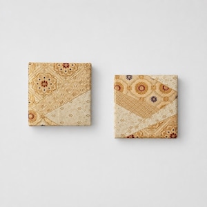 Puede incluir: Dos lienzos decorativos cuadrados con un diseño de patchwork. Los lienzos presentan una mezcla de telas beige, crema y marrón con estampados florales y geométricos. La estética general es vintage y elegante.