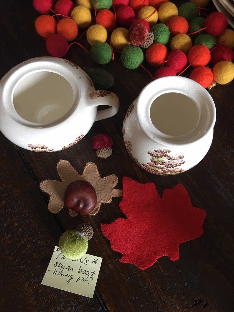 Puede incluir: Dos azucareros de cer&aacute;mica blanca con dise&ntilde;os florales marrones, una hoja de arce de fieltro rojo, una hoja de bellota de fieltro marr&oacute;n, una bellota de fieltro verde y una nota adhesiva amarilla con el texto "1/2 cups x sugar boat - honey pot."