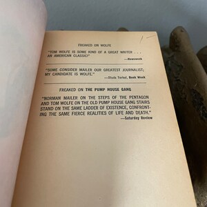 May include: A close-up of a book page with text about Tom Wolfe and Norman Mailer. The text quotes reviews of their work, calling them "great writers" and "journalists".