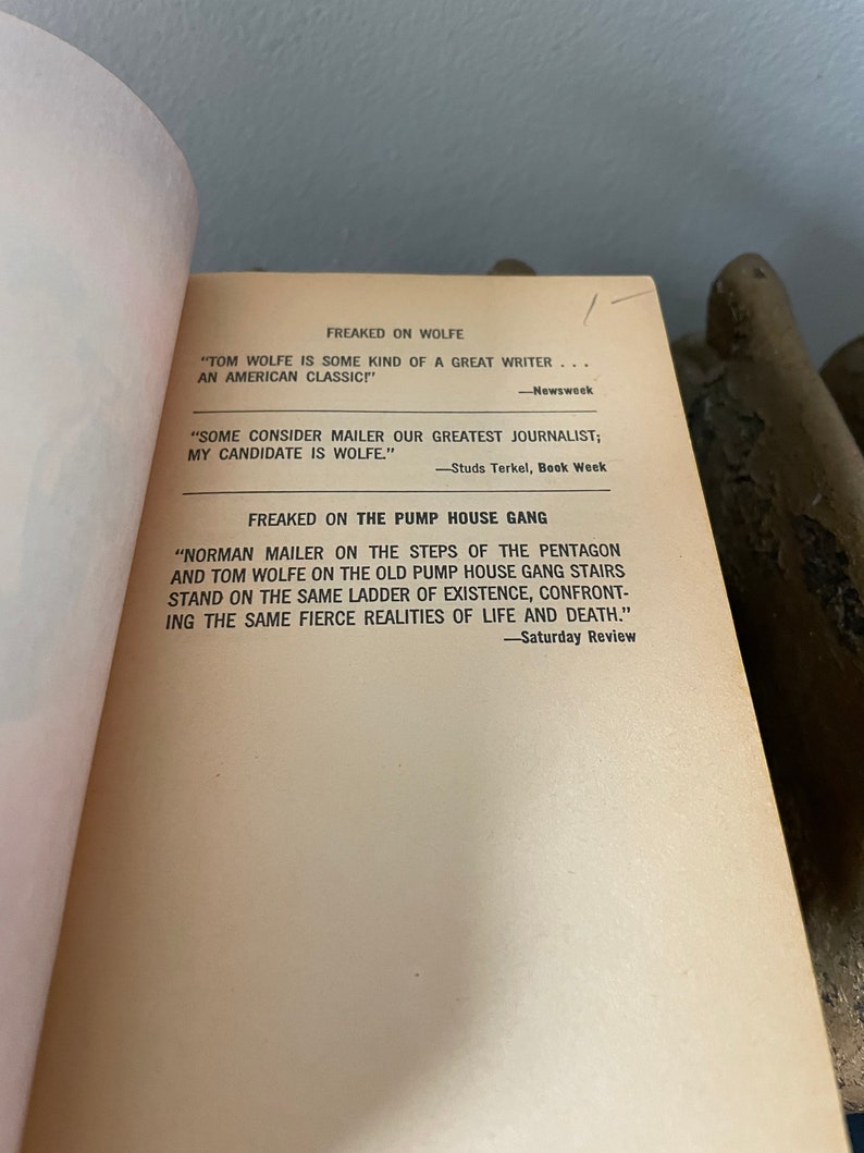 May include: A close-up of a book page with text about Tom Wolfe and Norman Mailer. The text quotes reviews of their work, calling them "great writers" and "journalists".