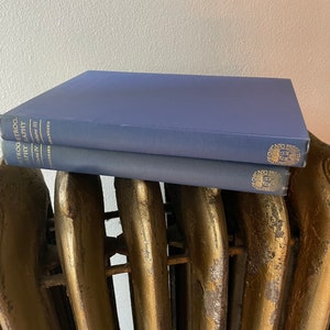 May include: Two navy blue hardcover books with gold lettering and a gold seal on the spine. The books are stacked on top of a gold-painted radiator.