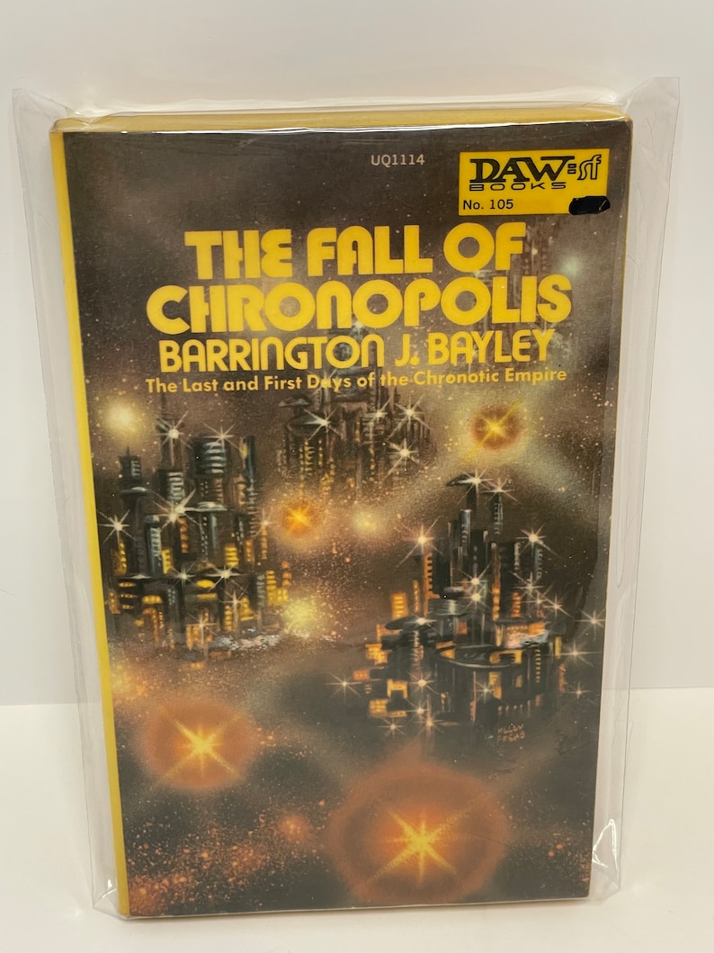 May include: A yellow and black paperback book with the title "The Fall of Chronopolis" by Barrington J. Bayley. The book cover features a futuristic city skyline with stars in the background. The book is a DAW Books publication, number 105.