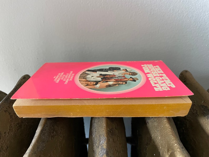 May include: A pink paperback book with a circle on the cover featuring a group of people. The title of the book is "The Pump House Gang" by Tom Wolfe.