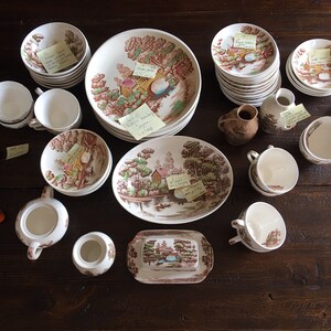 Puede incluir: Una colecci&oacute;n de tazas de t&eacute;, platillos y platos vintage con estampado floral marr&oacute;n y blanco. Tambi&eacute;n hay dos jarras de crema, un azucarero y una jarra. Los art&iacute;culos est&aacute;n dispuestos sobre una mesa de madera.