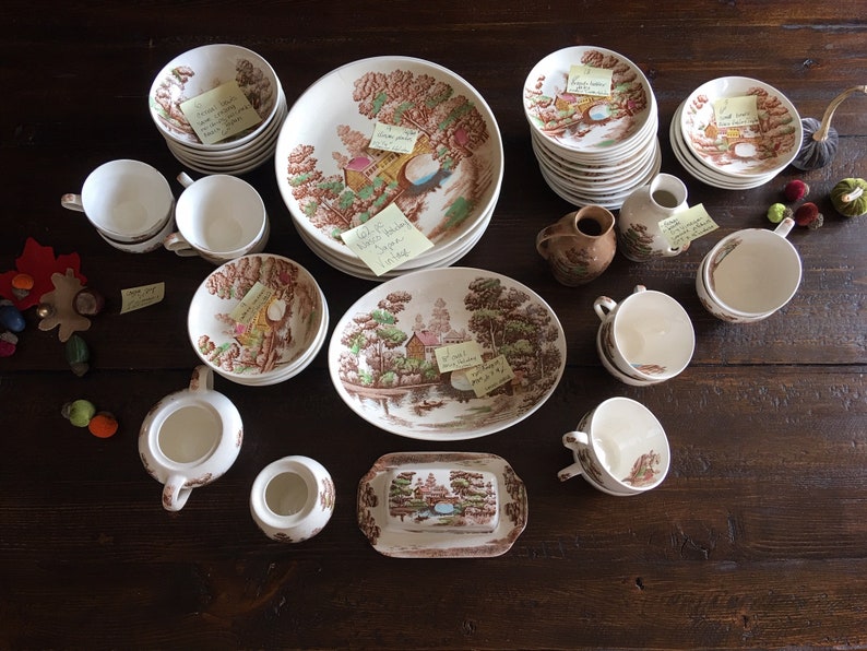 Puede incluir: Una colecci&oacute;n de tazas de t&eacute;, platillos y platos vintage con estampado floral marr&oacute;n y blanco. Tambi&eacute;n hay dos jarras de crema, un azucarero y una jarra. Los art&iacute;culos est&aacute;n dispuestos sobre una mesa de madera.