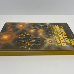May include: A paperback book cover with a dark background and a cityscape with stars. The title of the book is "The Fall of Chronopolis" by Barrington J. Bayley. The subtitle is "The Last and First Days of the Chrenatic Empire".