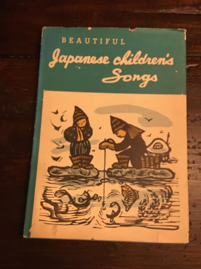 May include: A vintage book cover with a teal blue background and the title "Beautiful Japanese Children's Songs". The cover features an illustration of two children in winter clothing fishing in a frozen lake.